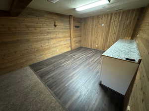 Empty room with a textured ceiling, wood walls, and wood finished floors