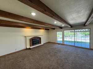 Unfurnished living room featuring a fireplace, a textured ceiling, baseboards, beamed ceiling, and dark colored carpet