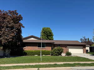 Ranch-style home with concrete driveway, a front yard, brick siding, and a garage