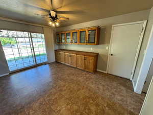 Kitchen with brown cabinetry, a textured ceiling, a ceiling fan, glass insert cabinets, and baseboards