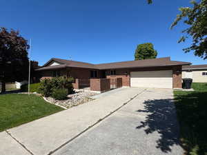Ranch-style home with a front yard, a garage, brick siding, and driveway
