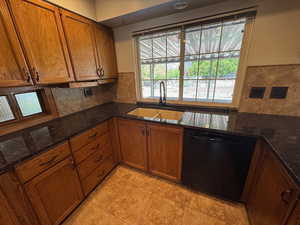 Kitchen with brown cabinetry, backsplash, black dishwasher, and a sink