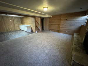 Unfurnished living room featuring a textured ceiling, visible vents, wood walls, stairway, and carpet floors