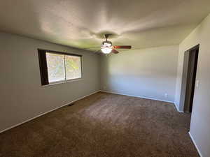 Empty room with a textured ceiling, dark colored carpet, a ceiling fan, and visible vents