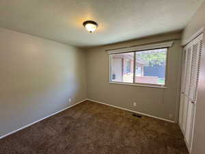 Spare room featuring baseboards, dark colored carpet, visible vents, and a textured ceiling