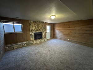 Unfurnished living room featuring wooden walls, a textured ceiling, and a stone fireplace
