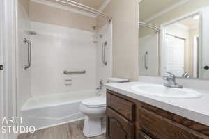 Full bath with toilet, wood finished floors, bathtub / shower combination, vanity, and ornamental molding