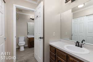 Bathroom with toilet, ornamental molding, visible vents, vanity, and wood finished floors