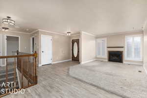 Unfurnished living room with ornamental molding, baseboards, a fireplace with flush hearth, and wood finished floors