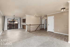 Unfurnished room with wood finished floors, a textured ceiling, baseboards, crown molding, and a notable chandelier