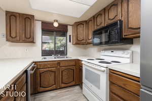 Kitchen with white electric stove, a sink, black microwave, light countertops, and light wood-type flooring