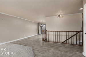 Spare room featuring a notable chandelier, a textured ceiling, baseboards, ornamental molding, and wood finished floors