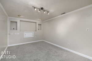 Carpeted spare room featuring crown molding, a textured ceiling, visible vents, and baseboards