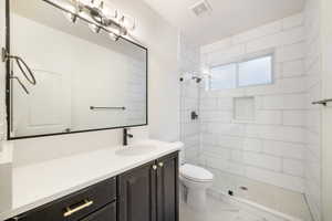 Bathroom with toilet, marble finish floor, visible vents, tiled shower, and vanity