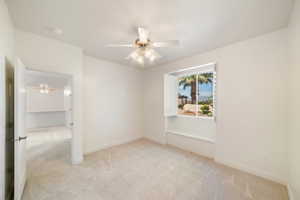 Spare room with light colored carpet, baseboards, and a ceiling fan