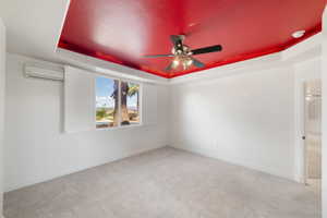 Spare room featuring carpet floors, a wall unit AC, a ceiling fan, a tray ceiling, and baseboards