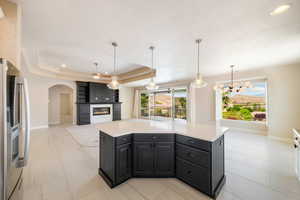 Kitchen featuring baseboards, stainless steel refrigerator with ice dispenser, arched walkways, light countertops, and a large fireplace