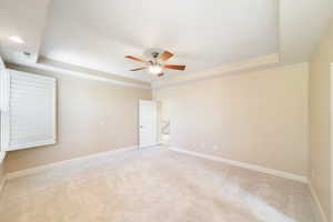 Carpeted spare room featuring a ceiling fan, a raised ceiling, and baseboards