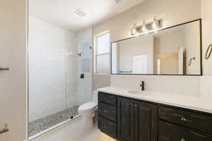 Bathroom featuring toilet, vanity, visible vents, tile patterned flooring, and tiled shower
