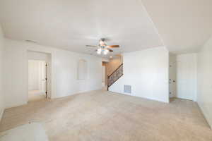 Unfurnished living room featuring light colored carpet, stairway, a ceiling fan, and visible vents