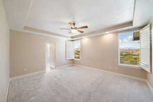 Carpeted spare room featuring a tray ceiling, baseboards, and a ceiling fan