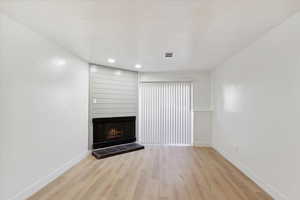 Unfurnished living room featuring visible vents, light wood-style floors, baseboards, and a fireplace