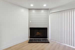 Room details with baseboards, a fireplace with raised hearth, recessed lighting, and wood finished floors