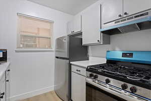 Kitchen with stainless steel appliances, under cabinet range hood, light countertops, white cabinetry, and light wood finished floors