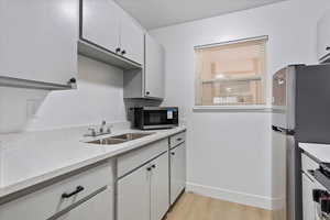 Kitchen featuring a sink, stainless steel appliances, light wood-type flooring, baseboards, and white cabinetry