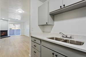 Kitchen with a sink, light wood-type flooring, gray cabinets, light stone countertops, and a fireplace