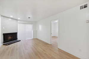 Unfurnished living room featuring baseboards, a large fireplace, light wood-style flooring, and visible vents