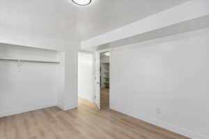 Unfurnished bedroom featuring a textured ceiling, baseboards, a closet, and light wood-style flooring