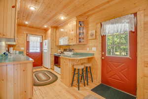 Kitchen featuring white appliances, wood ceiling, wood walls, a kitchen breakfast bar, and light wood-type flooring