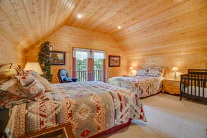 Bedroom with vaulted ceiling, wood walls, wooden ceiling, and access to exterior