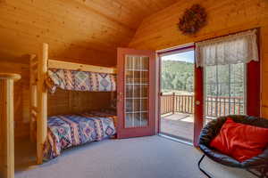 Carpeted bedroom with vaulted ceiling, wooden ceiling, wooden walls, and access to outside