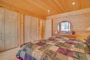 Bedroom featuring recessed lighting, wood ceiling, wooden walls, two closets, and wood finished floors
