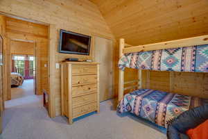 Bedroom with vaulted ceiling, wooden walls, carpet floors, and wooden ceiling