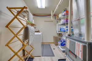 Clothes washing area with laundry area, heating unit, independent washer and dryer, and light wood-style floors