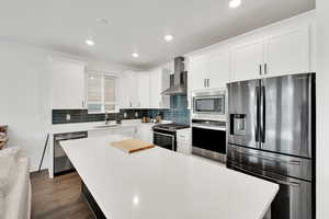 Kitchen with light countertops, wall chimney exhaust hood, stainless steel appliances, and a sink