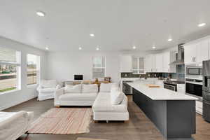 Kitchen with a sink, wall chimney range hood, open floor plan, plenty of natural light, and appliances with stainless steel finishes