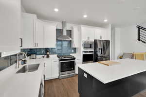 Kitchen featuring wall chimney range hood, appliances with stainless steel finishes, decorative backsplash, and a sink