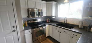 Kitchen with a sink, white cabinetry, dark countertops, tasteful backsplash, and appliances with stainless steel finishes