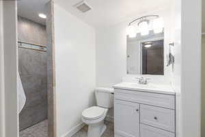 Bathroom featuring a tile shower, toilet, vanity, and baseboards