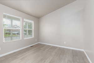 Empty room featuring light wood-style floors, baseboards, and vaulted ceiling