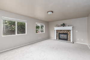 Unfurnished living room featuring carpet floors, baseboards, and a stone fireplace
