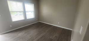 Spare room with baseboards, visible vents, and dark wood-type flooring