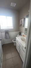 Half bath featuring toilet, vanity, visible vents, tile patterned flooring, and wainscoting