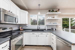 Kitchen with stainless steel appliances, a sink, backsplash, dark countertops, and white cabinets