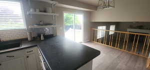 Kitchen with light wood-style flooring, white cabinets, open shelves, dark countertops, and tasteful backsplash