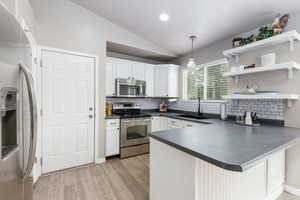 Kitchen with appliances with stainless steel finishes, a sink, dark countertops, lofted ceiling, and decorative backsplash